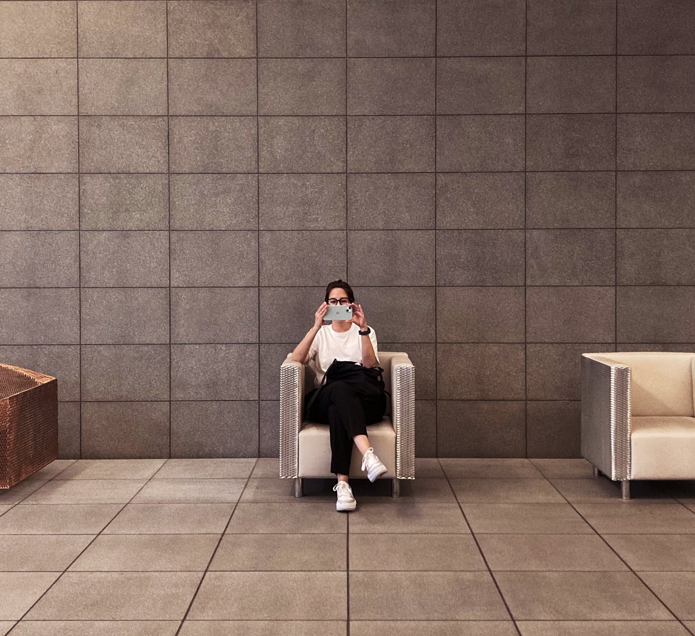 Portrait of Gisela Trujillo wearing glasses and a white shirt, seated against a modern tiled wall.