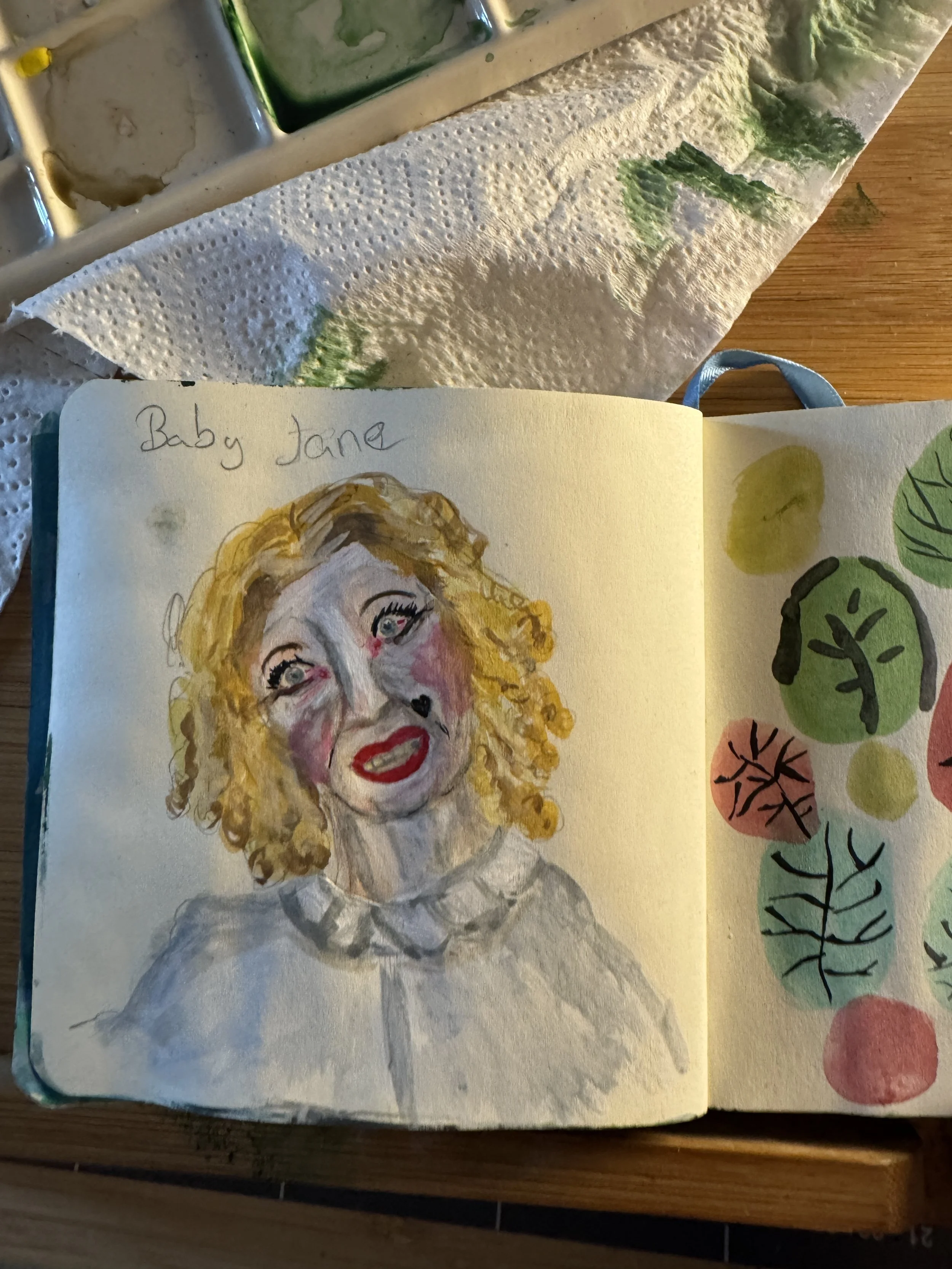 Sketch of a woman with curly blonde hair labeled "Baby Jane" with colorful painted face and clothing, next to a page of abstract green and pink leaves and circles.