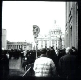 Black and white photo of a busy city street with people walking and a historic building in the background.