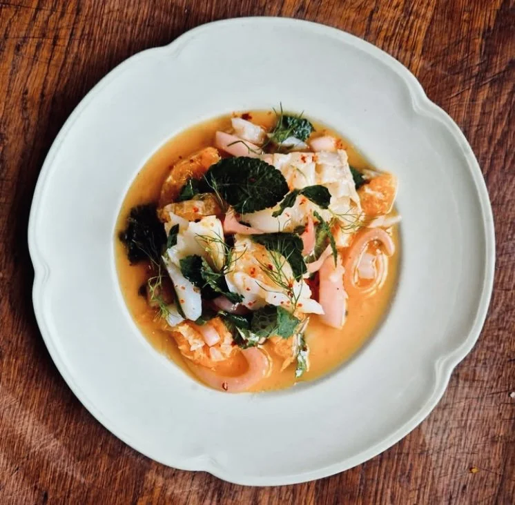 A white bowl filled with seafood, herbs, and sauce on a wooden surface.