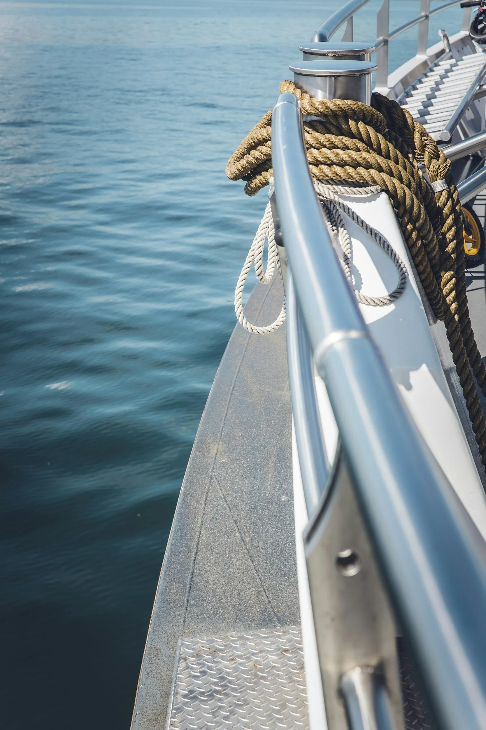 Close-up of a boat's metal railing with coiled ropes tied around the posts, on a body of water with gentle ripples.