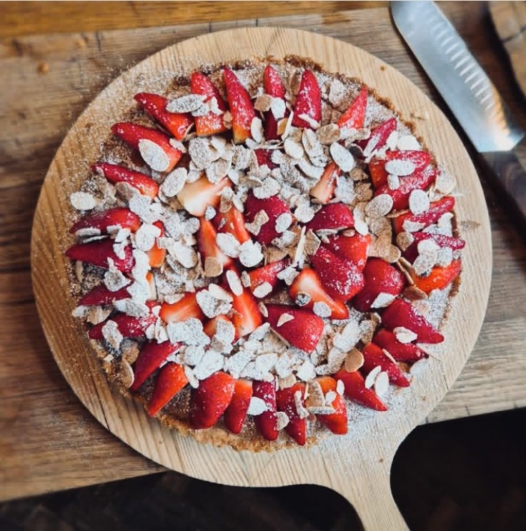 Strawberry tart topped with sliced strawberries, slivered almonds, and powdered sugar on a wooden serving board.