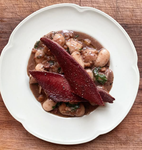 A white plate with a serving of chicken and mushroom stew topped with two slices of cooked beetroot on a wooden table.