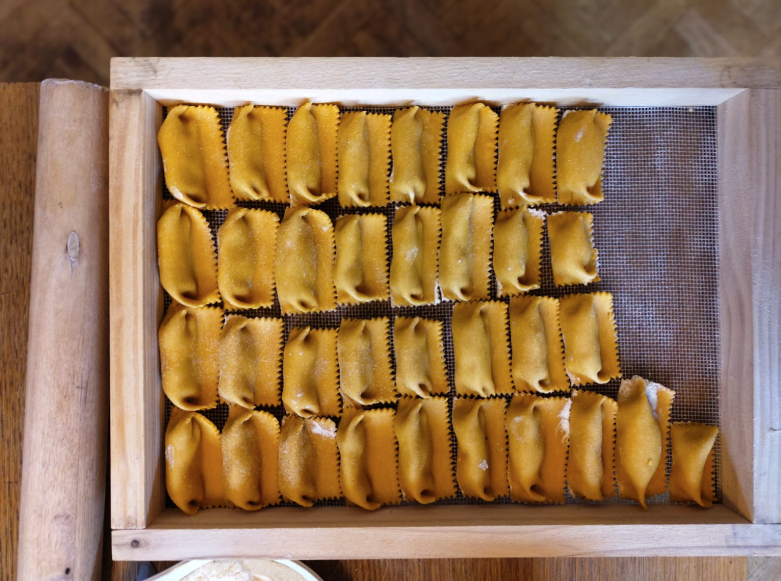 Tray of uncooked ravioli pasta on a wooden surface.