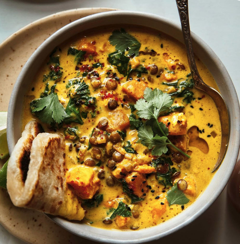 A bowl of Indian-style yellow lentil curry with chunks of sweet potatoes, garnished with cilantro and served with toasted pita bread.