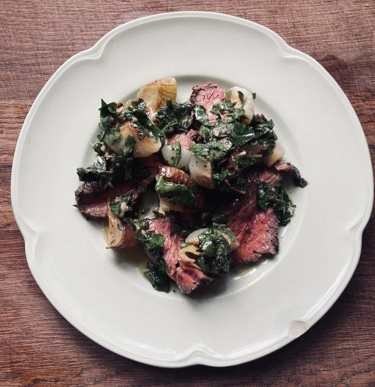 Steak and greens on a white plate with sauce and diced onions