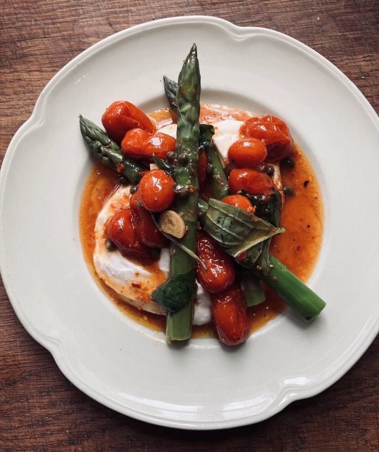 A plate with cherry tomatoes, green beans, and leafy herbs in a tomato-based sauce over a poached egg.