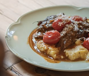 Savory dish with mashed potatoes topped with braised beef, cherry tomatoes, and grated cheese, served on a light green plate.