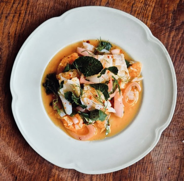 A plate of seafood chowder garnished with fresh herbs on a wooden table.