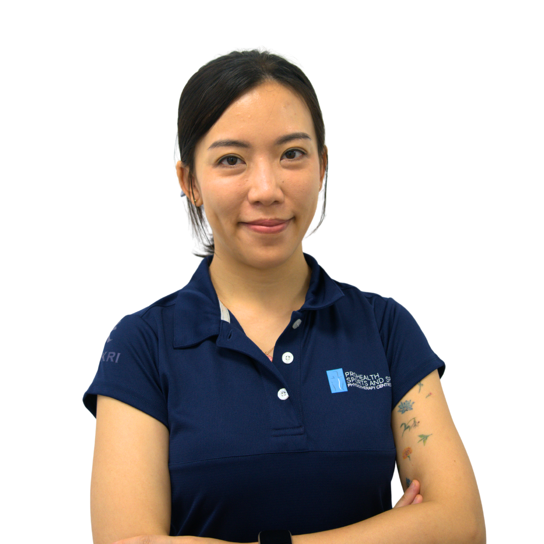 A woman with dark hair in a blue polo shirt, standing against a white background, with her arms crossed and looking at the camera.