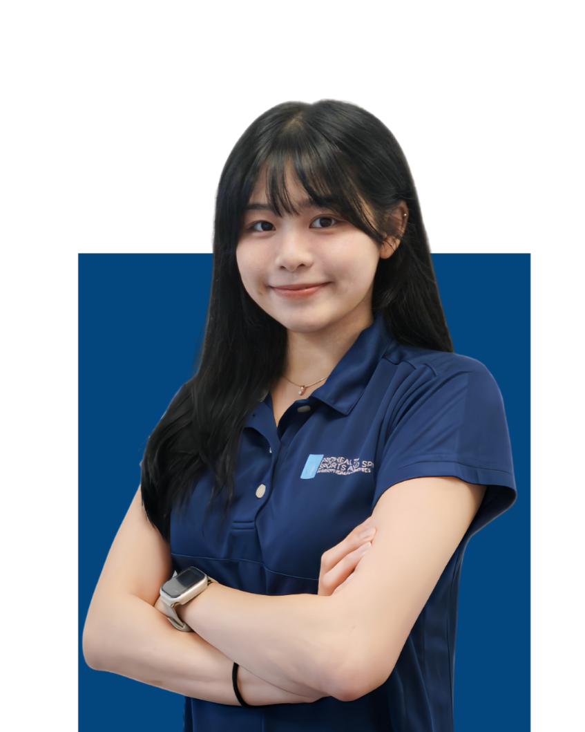 A young woman with long black hair wearing a navy polo shirt with an embroidered logo, standing with her arms crossed and smiling, against a blue and white background.