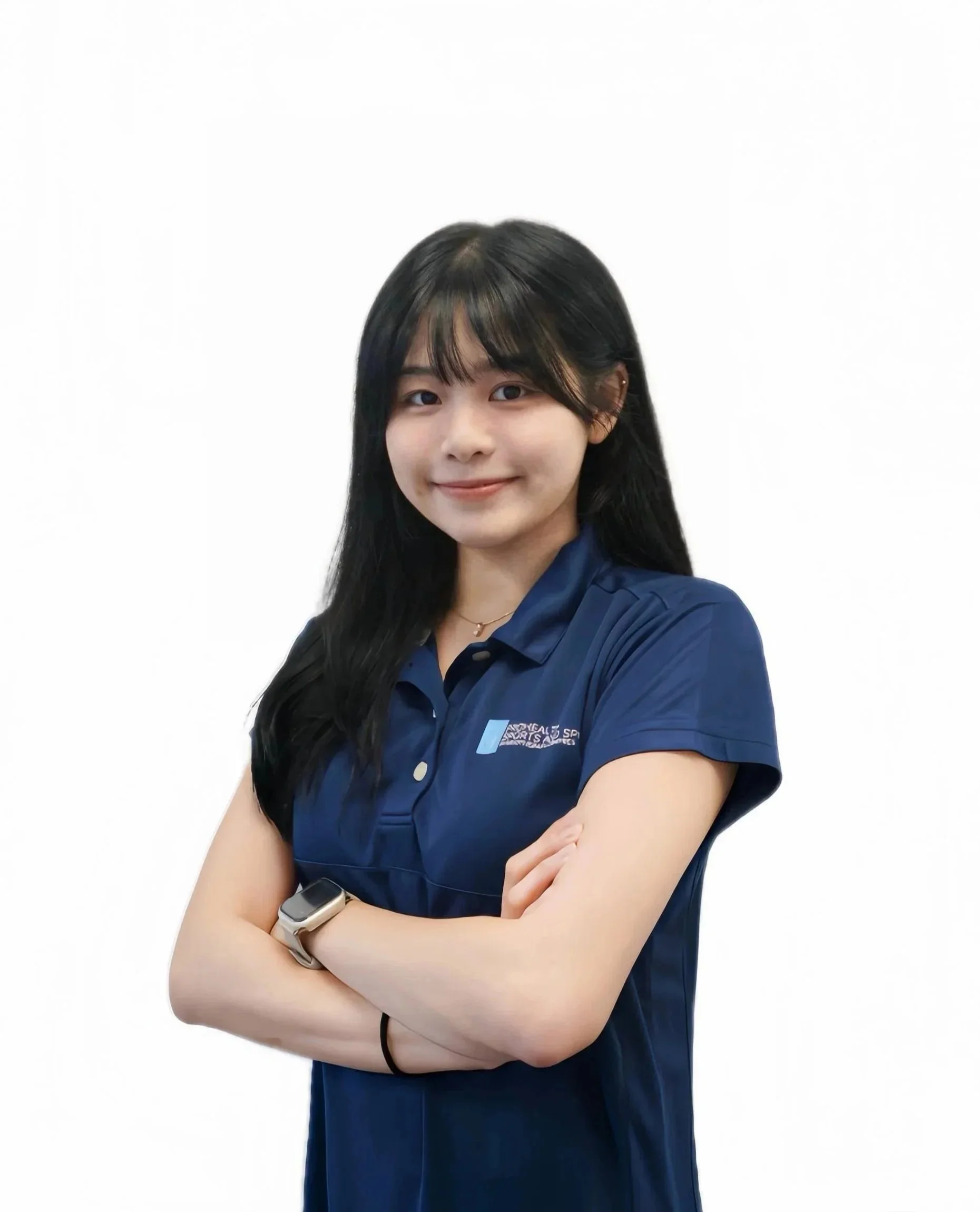 Young woman with dark hair wearing a blue polo shirt, arms crossed, smiling, standing against a white background.