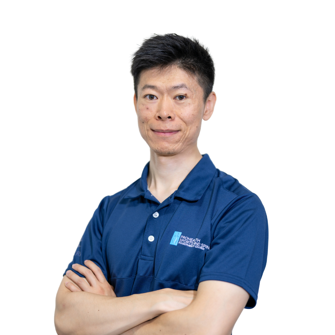 A man with short black hair and light skin, wearing a navy blue polo shirt with a logo on the chest, crossed arms, smiling slightly, standing against a white background.