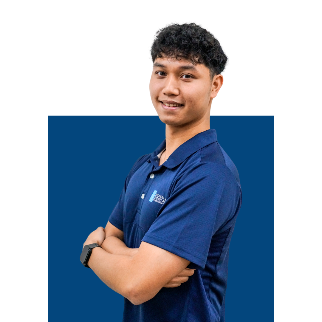 Young man with curly black hair smiling, wearing a blue polo shirt with logo, standing with arms crossed against a white background