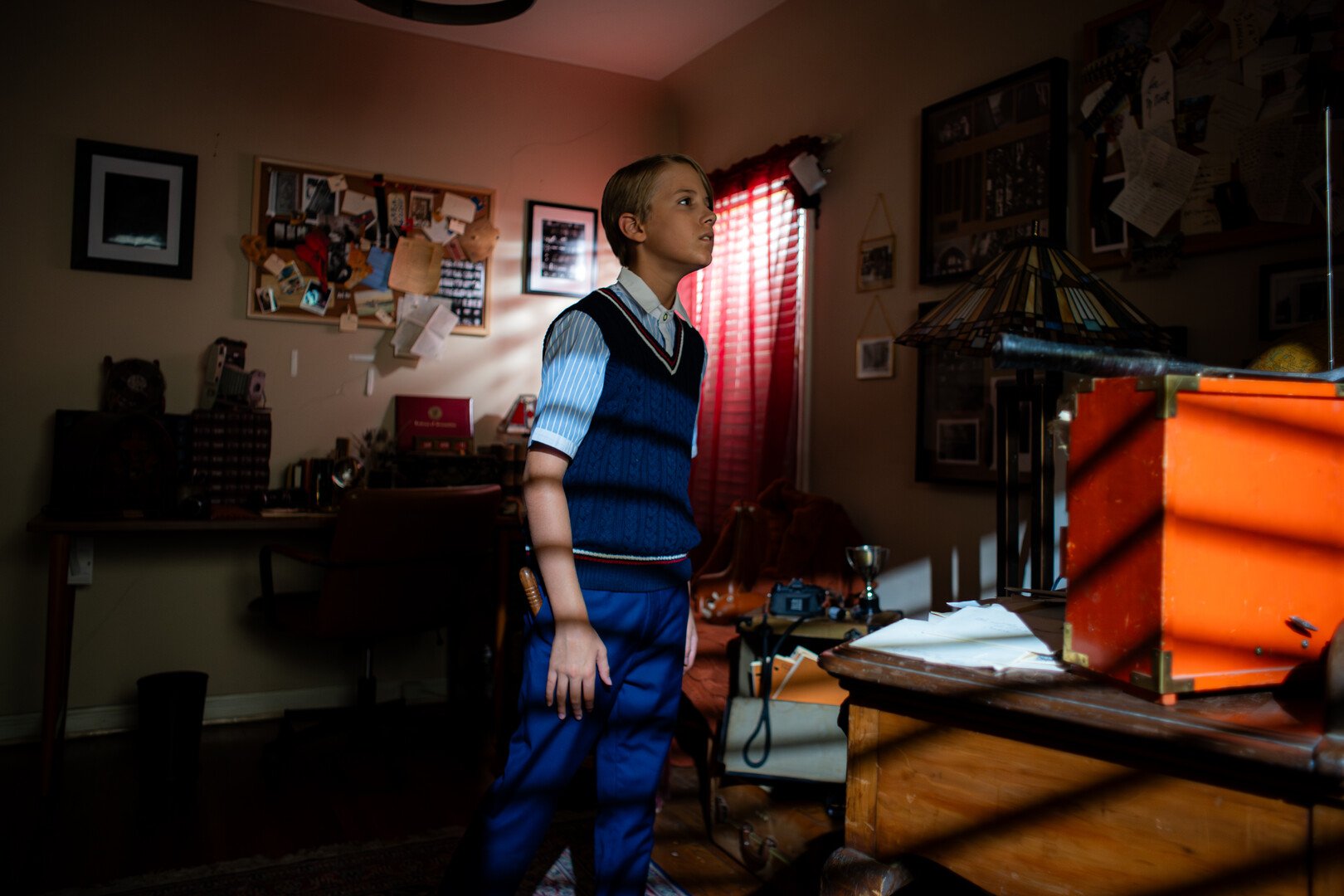 A young boy, stands in the living room, he is transfixed by something off camera, perhaps a memory, something has caught his attention.