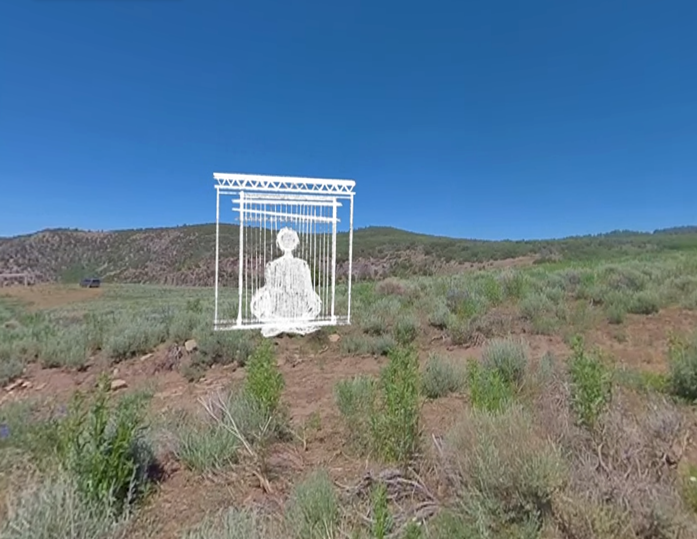 A hand-drawn caged figure sits in a real photographed and filmed desert landscape, with green shrubs and brown bushes.