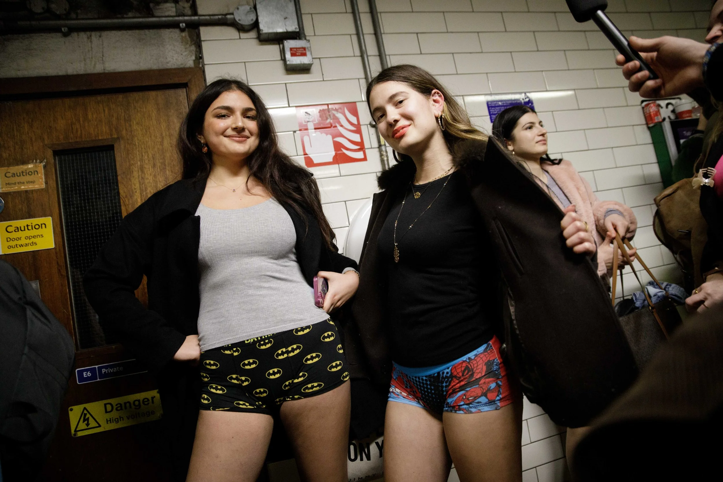 2 women pose in superhero underwear on the station platform for the No Trousers Tube Ride 2026. An annual event in which participants ride the tube around London whilst only wearing their underwear on their lower half. An event hosting and organised 