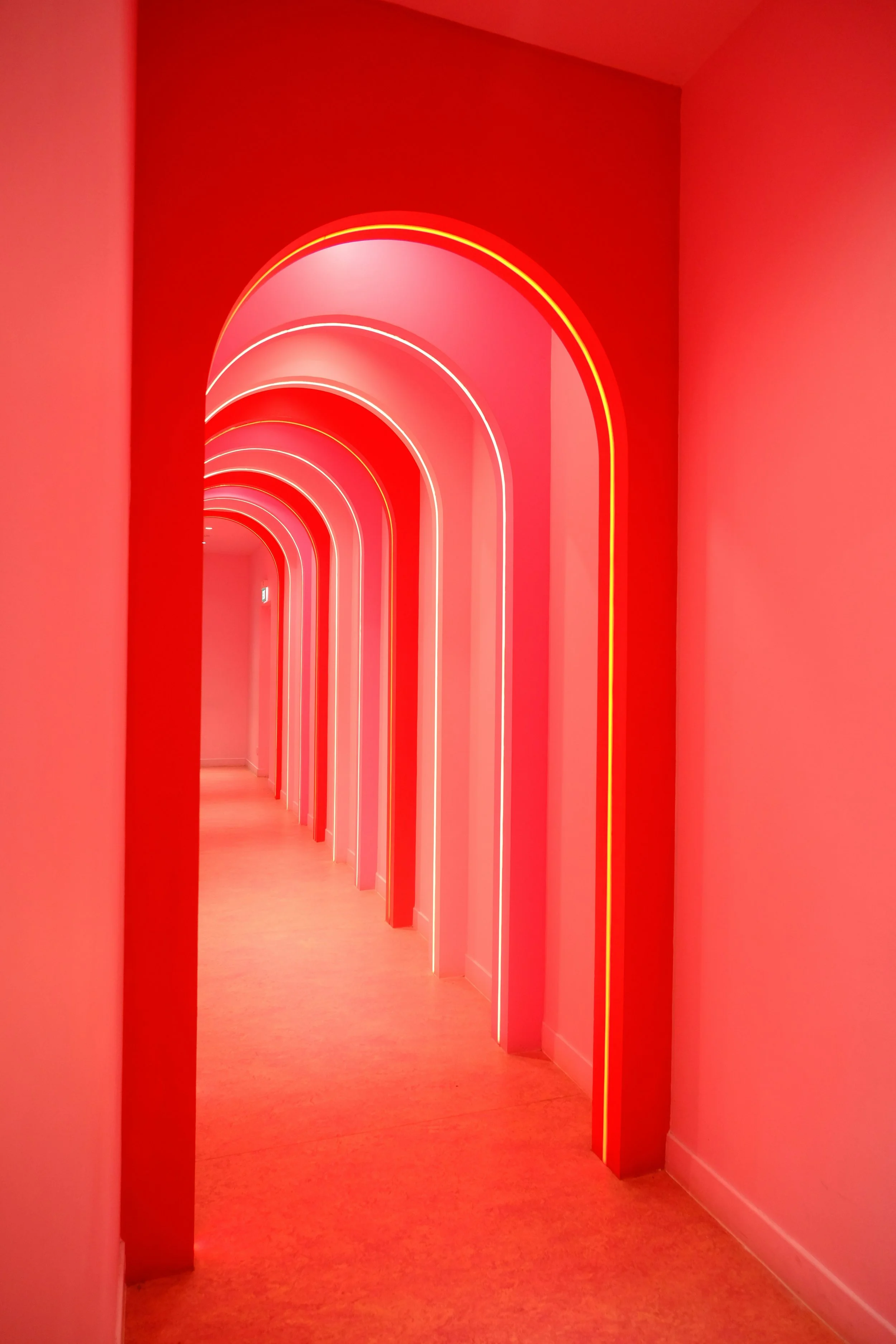 A hallway with multiple pink archways illuminated by neon lights, creating a vibrant, modern atmosphere.