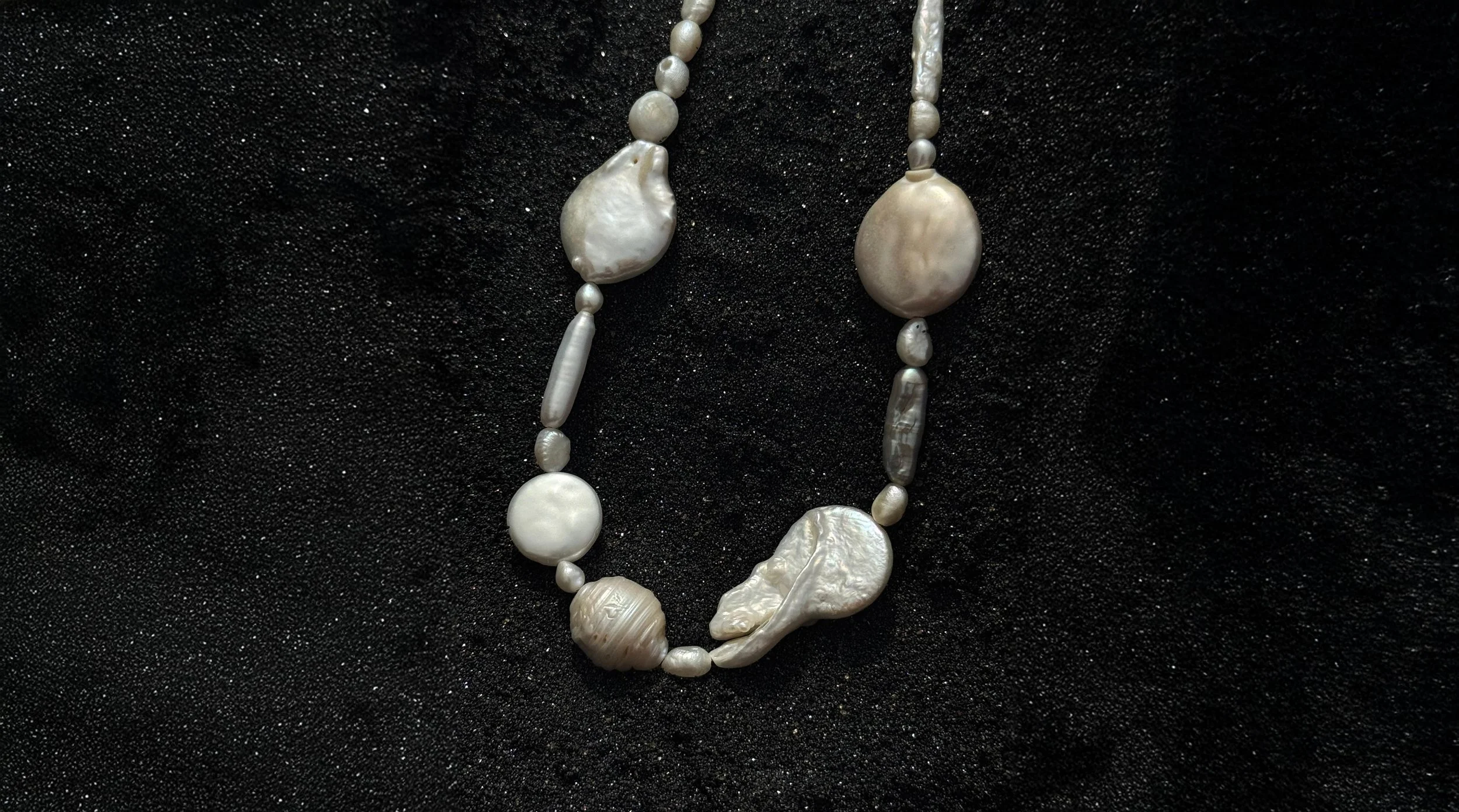 A necklace made of white pearls and beads displayed on black fabric.