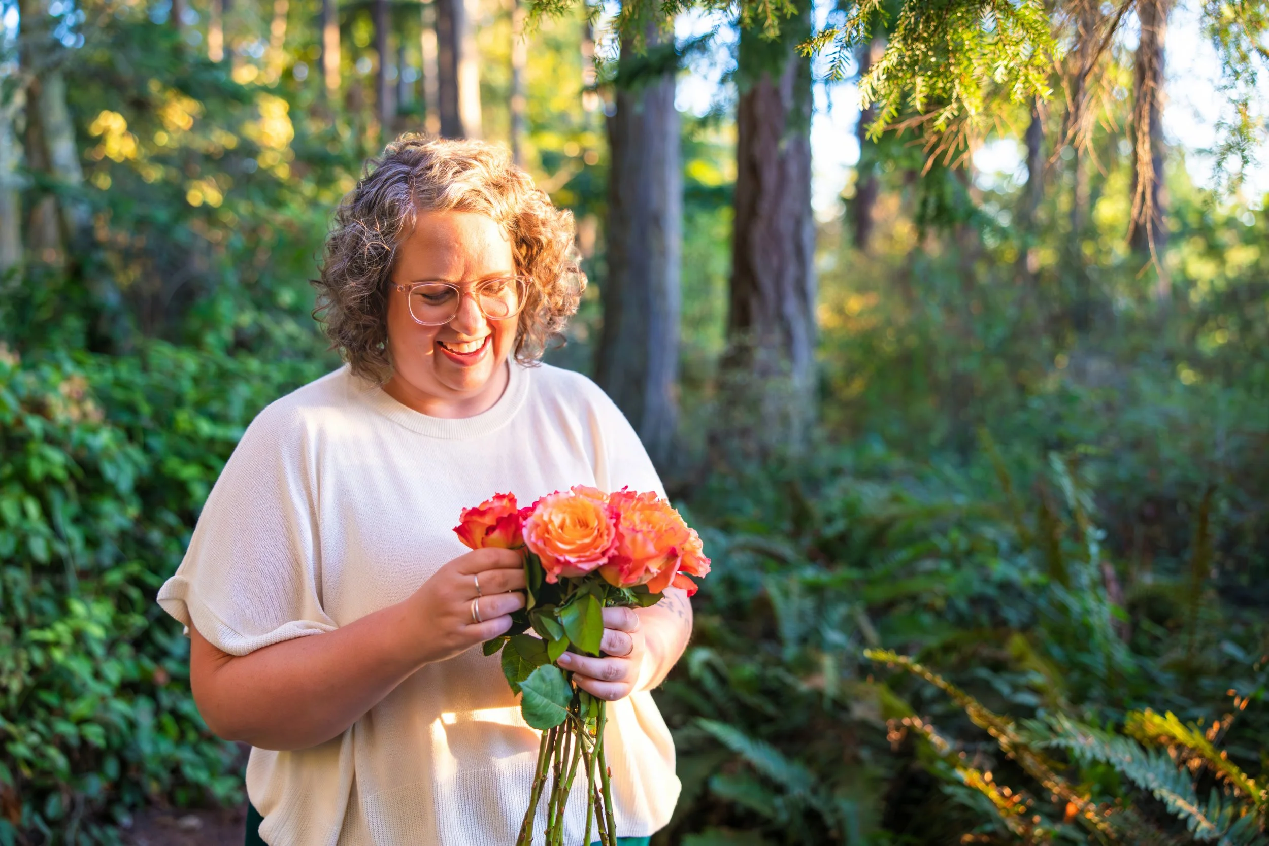 Annie Mesaros smiling and holding a bouquet of roses in the woods.