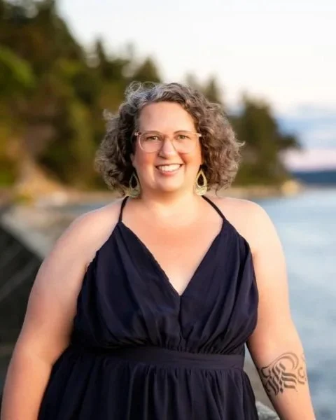 Annie Mesaros, spiritual counselor and founder of Wild Maven Wellness, smiling outdoors by the water.