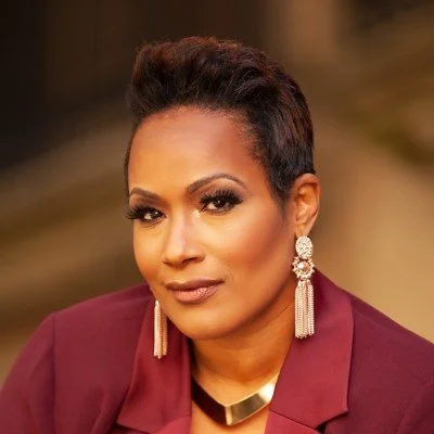 Portrait of a woman with short hair wearing a burgundy blazer and statement earrings, looking confidently at the camera.