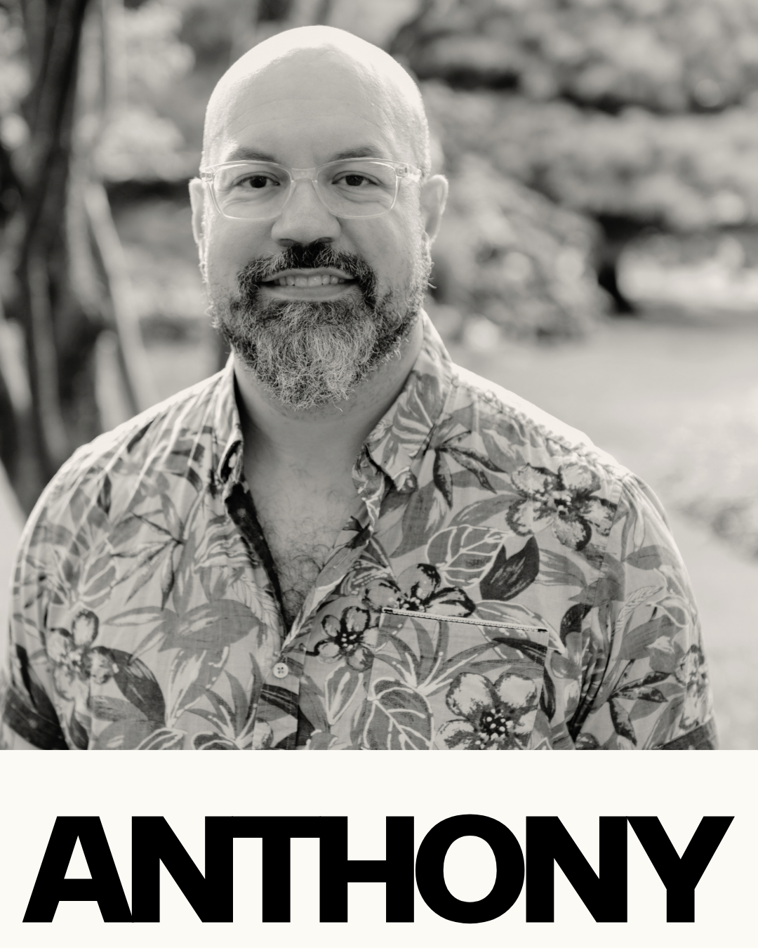 Black and white portrait of a man with a beard, glasses, and a shaved head, wearing a floral shirt, outdoors with trees in the background, and the name 'Anthony' in bold letters at the bottom.