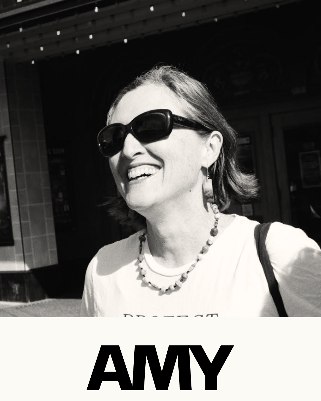 Black and white photo of a woman wearing sunglasses, smiling outdoors with the name 'AMY' written underneath.
