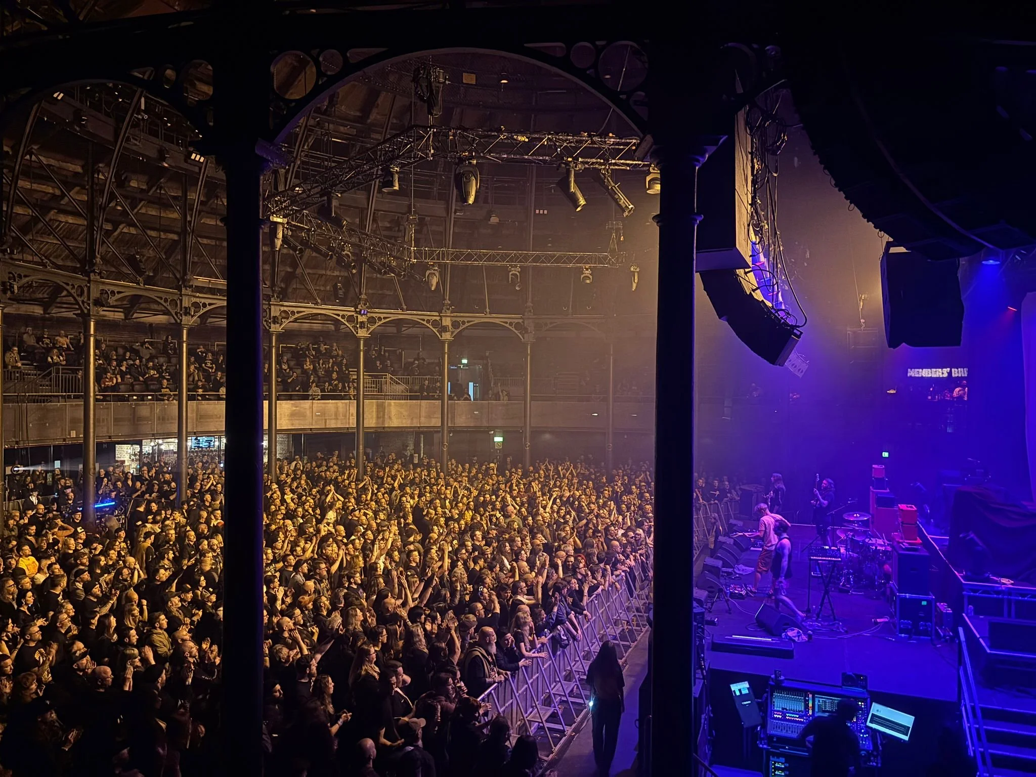 Indoor concert venue filled with audience watching a performance on stage with lighting and sound equipment visible.