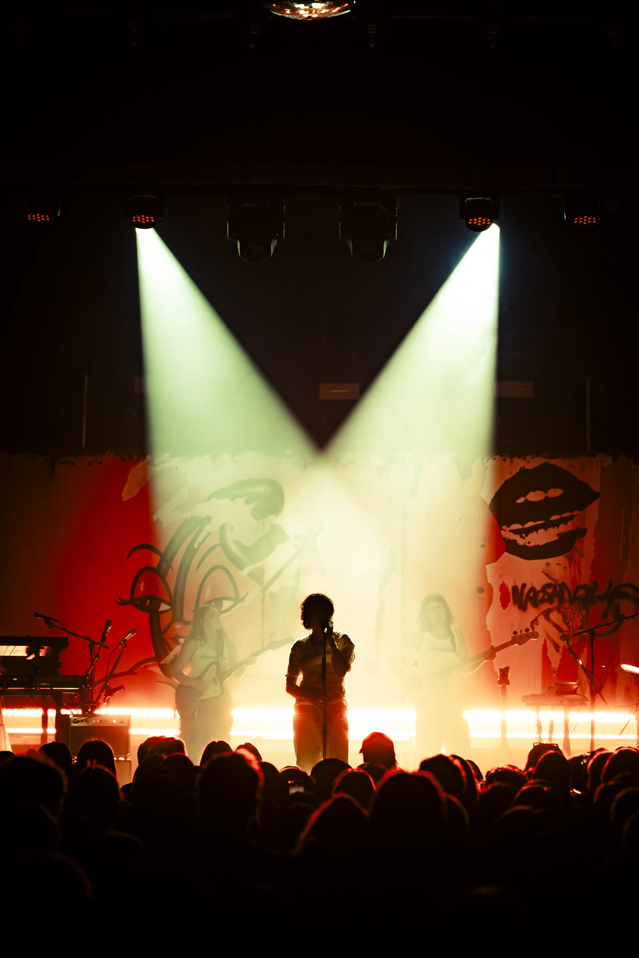 A live music performance on stage with multiple band members, colorful backdrops, and spotlights illuminating the performers.