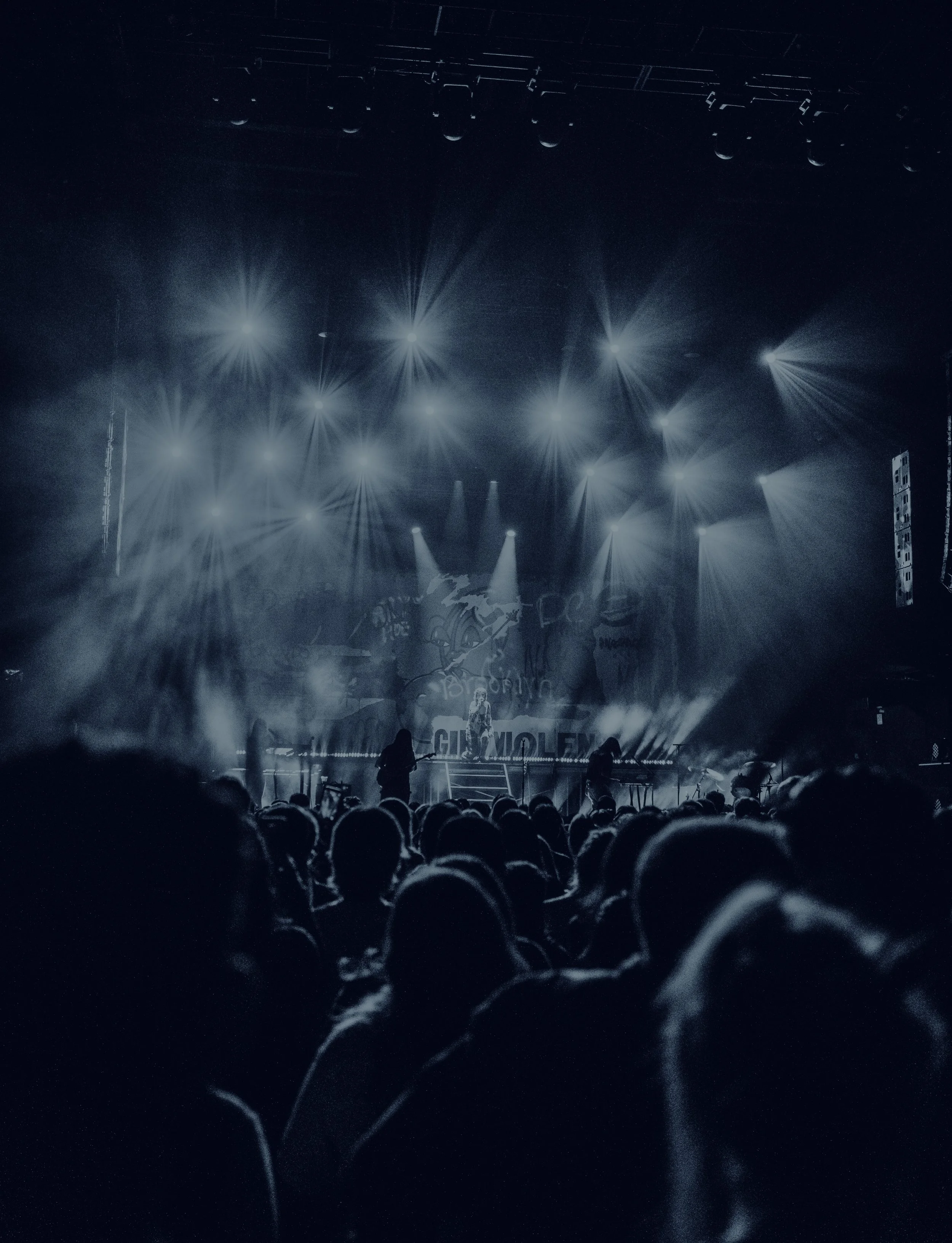 Concert stage with bright lights, fog, and silhouettes of an audience watching a performance.