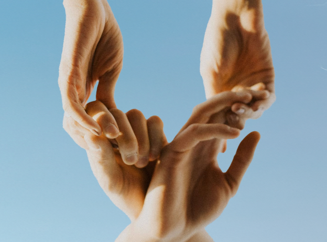 Mãos humanas formando um coração contra um background azul.