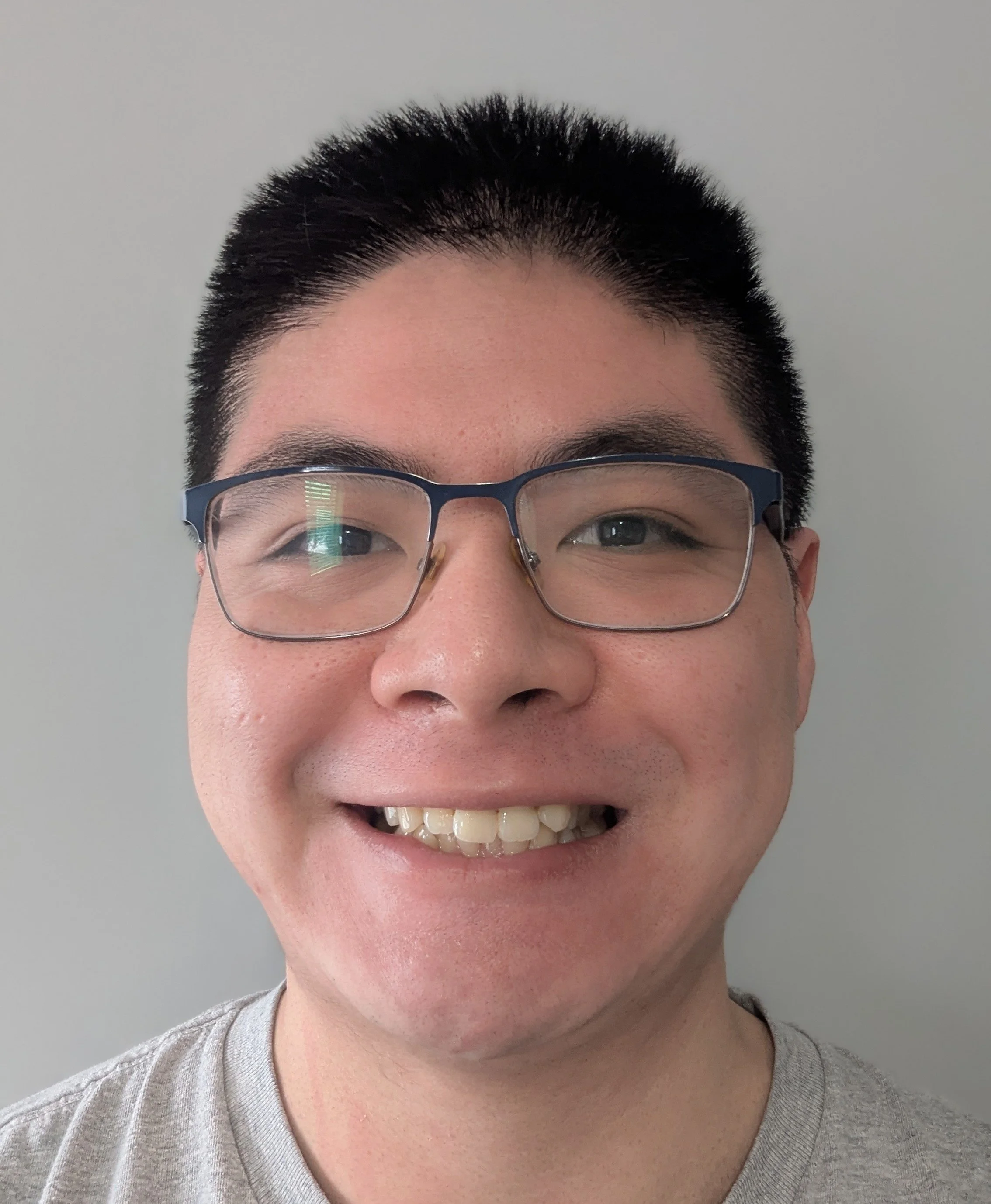Close-up of a smiling person with black hair, glasses, and a gray shirt, against a plain light gray background. - web designer toronto,  web designer canada, web design toronto, design toronto web,