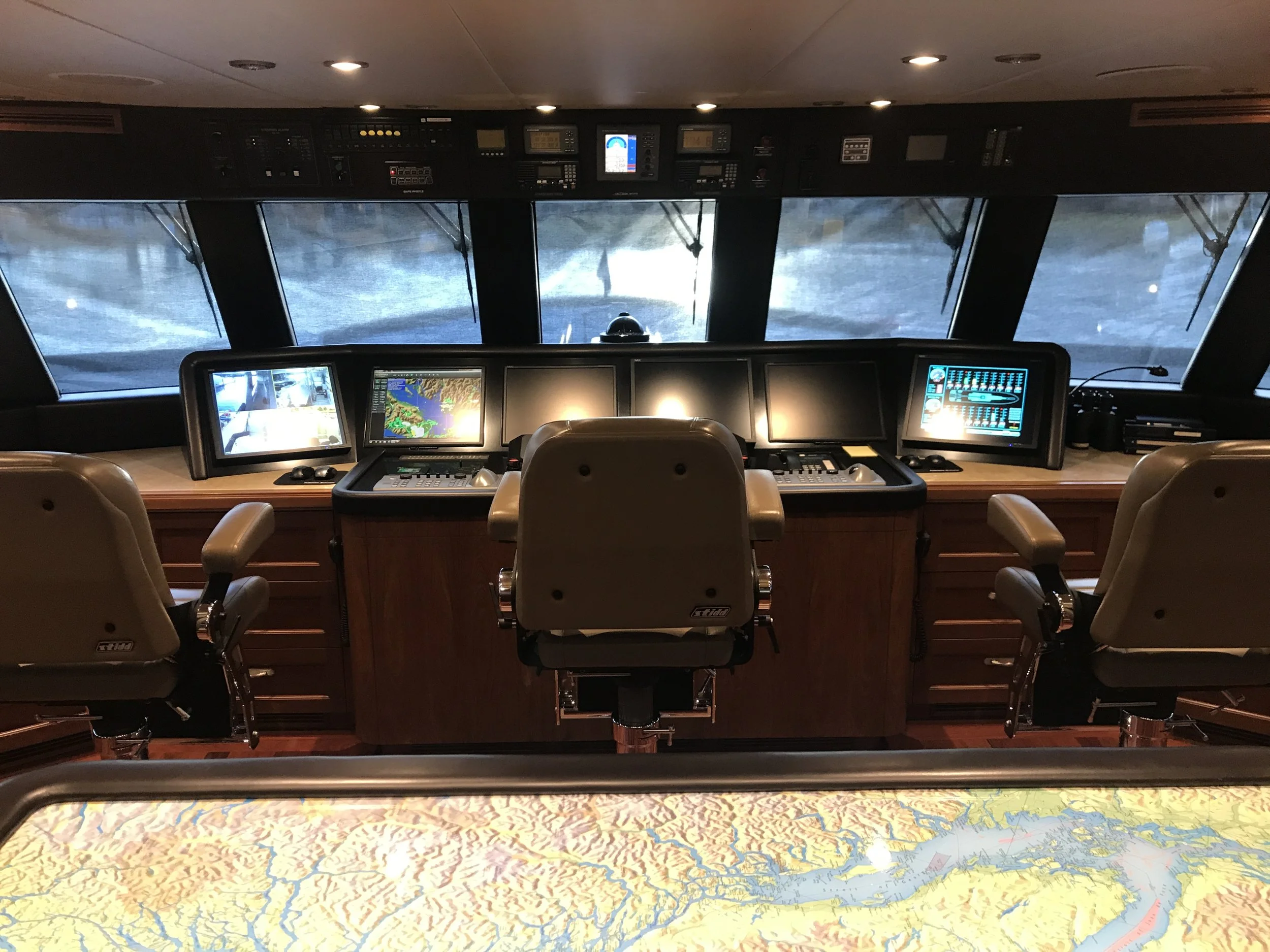View from the ship's cockpit or bridge showing navigation and communication equipment, large windows with a view of water and ice, and a map below indicating the ship's location.