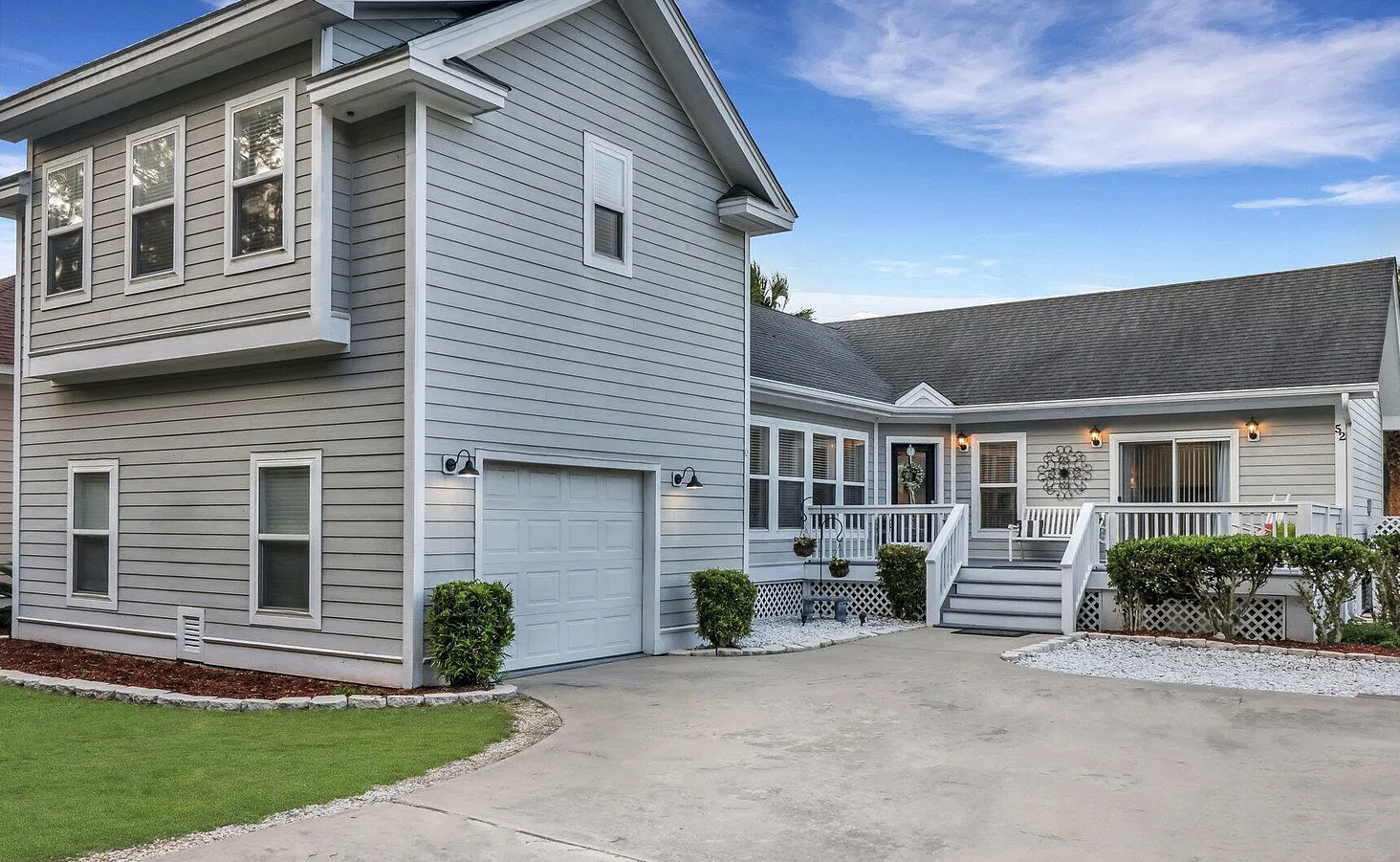 Modern gray two-story house with white trim, large driveway, attached garage, and manicured landscaping.