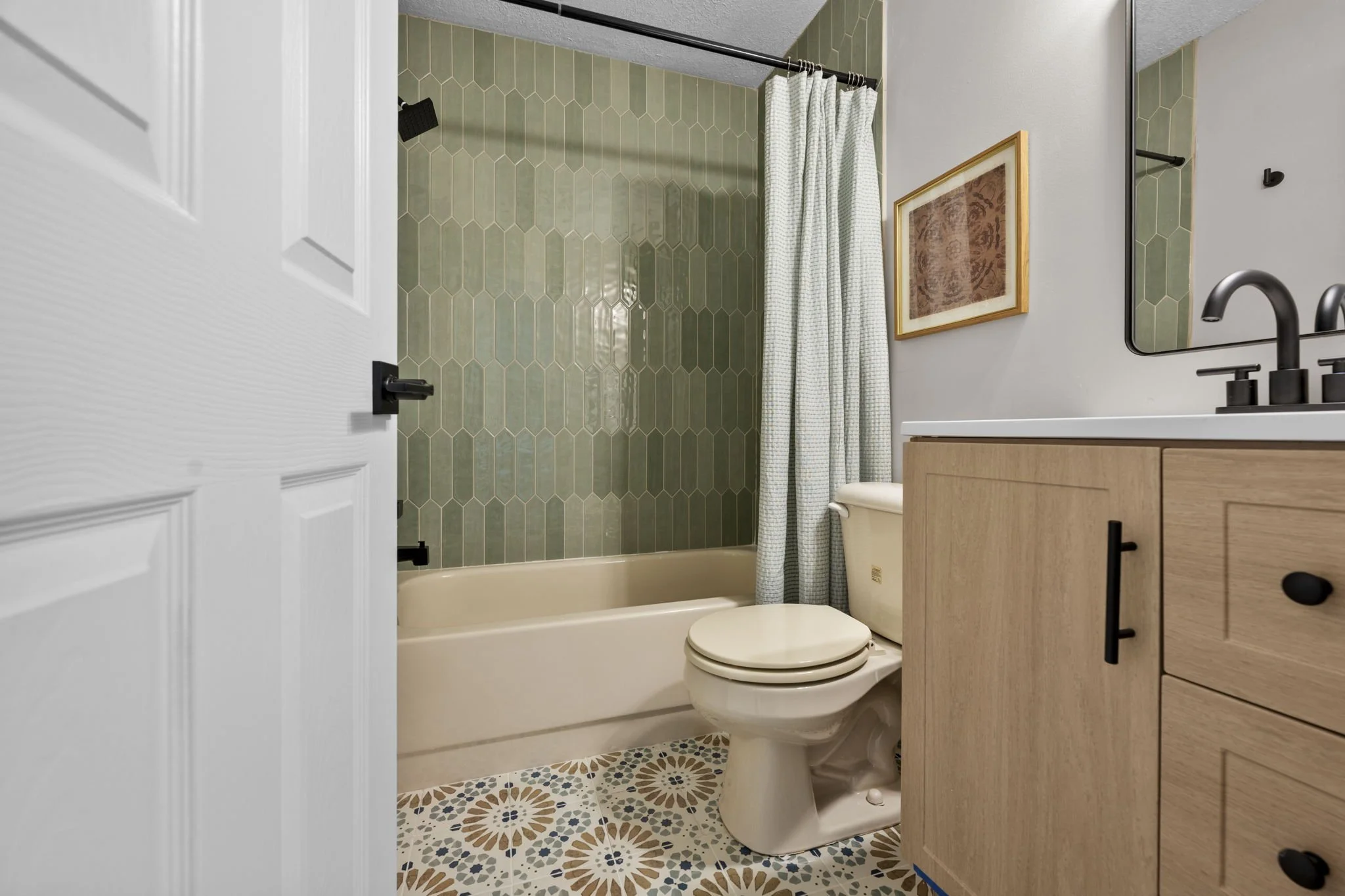 Bathroom renovation featuring vertical green tile, patterned flooring, warm wood vanity, and updated fixtures designed to bring character and function to a compact space.