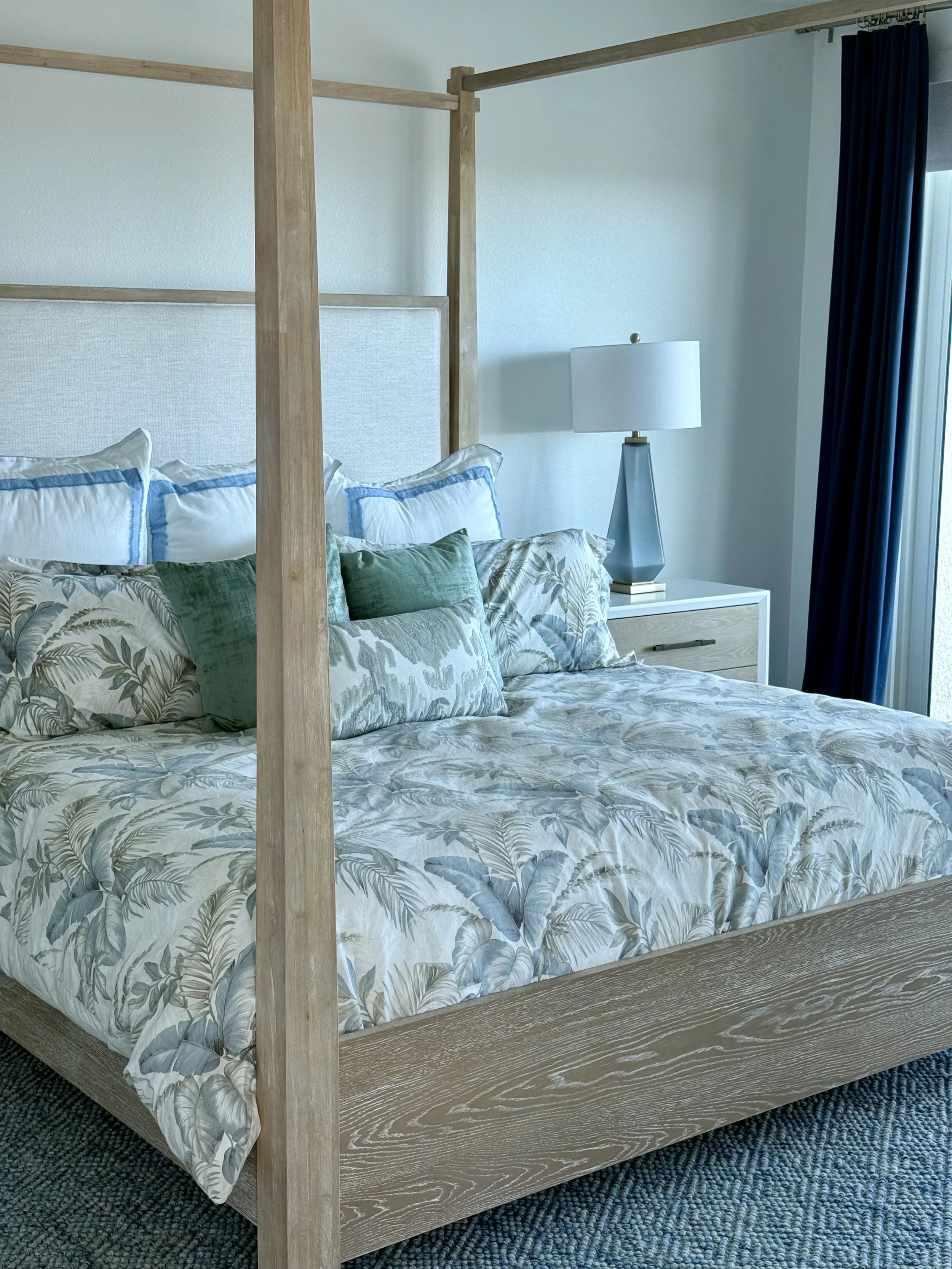 Coastal primary bedroom featuring a light wood canopy bed, layered textiles, and calming blue accents overlooking Clearwater Beach.