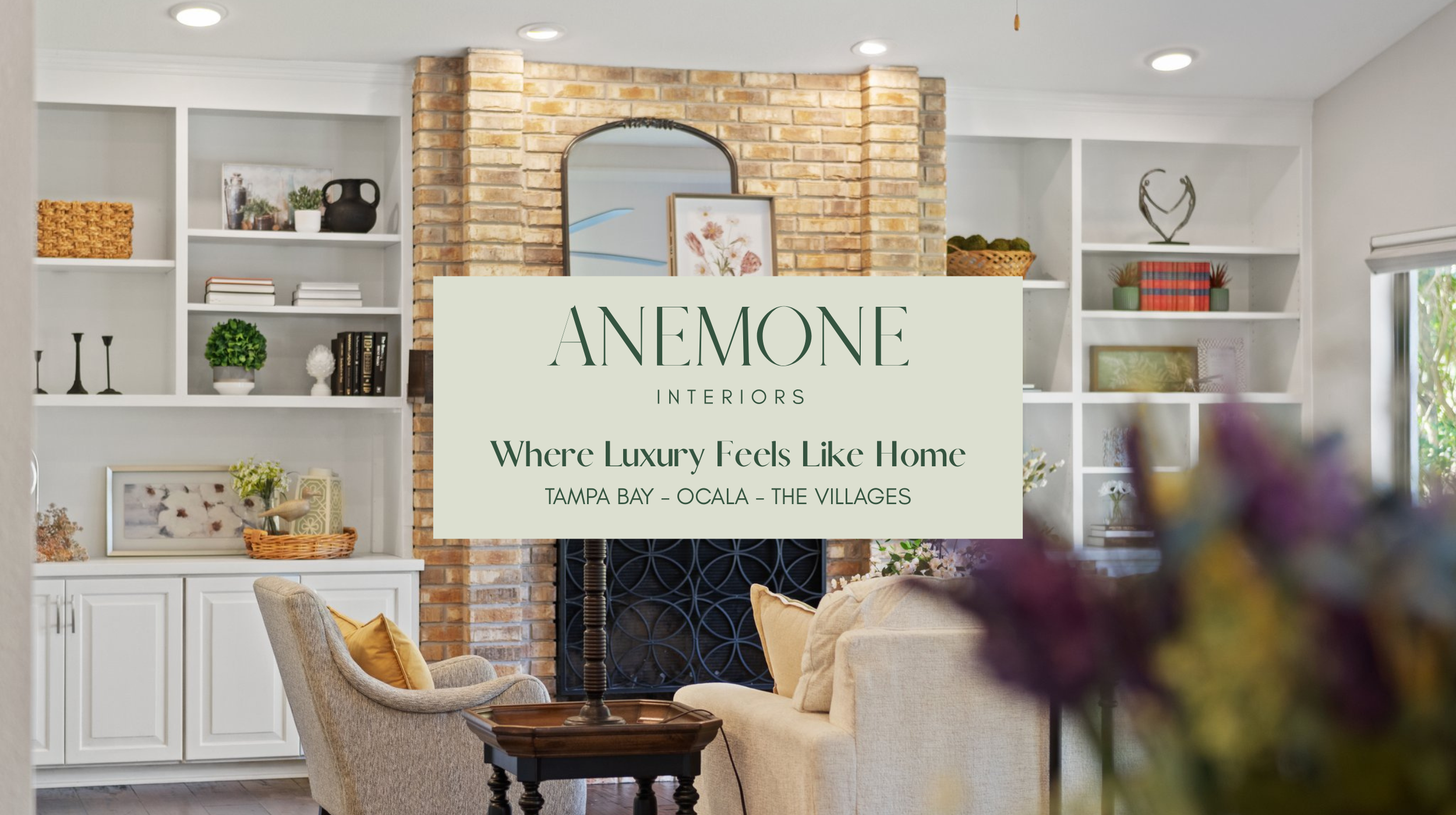 Modern living room interior design by Anemone Interiors featuring custom white built-ins, exposed brick fireplace, layered neutral furnishings, and warm organic styling in a Tampa Bay luxury home.