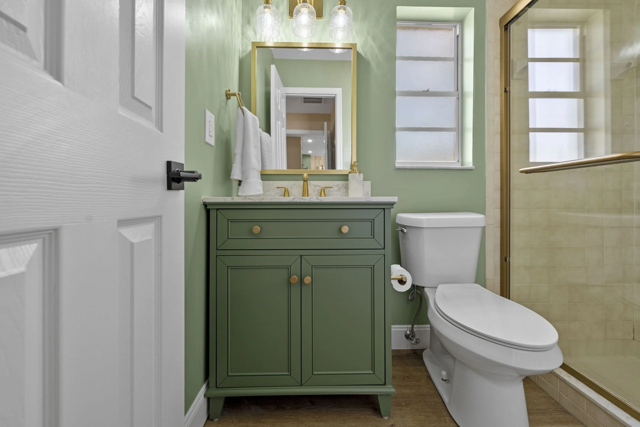 Bathroom renovation featuring vertical green tile, patterned flooring, warm wood vanity, and updated fixtures designed to bring character and function to a compact space.