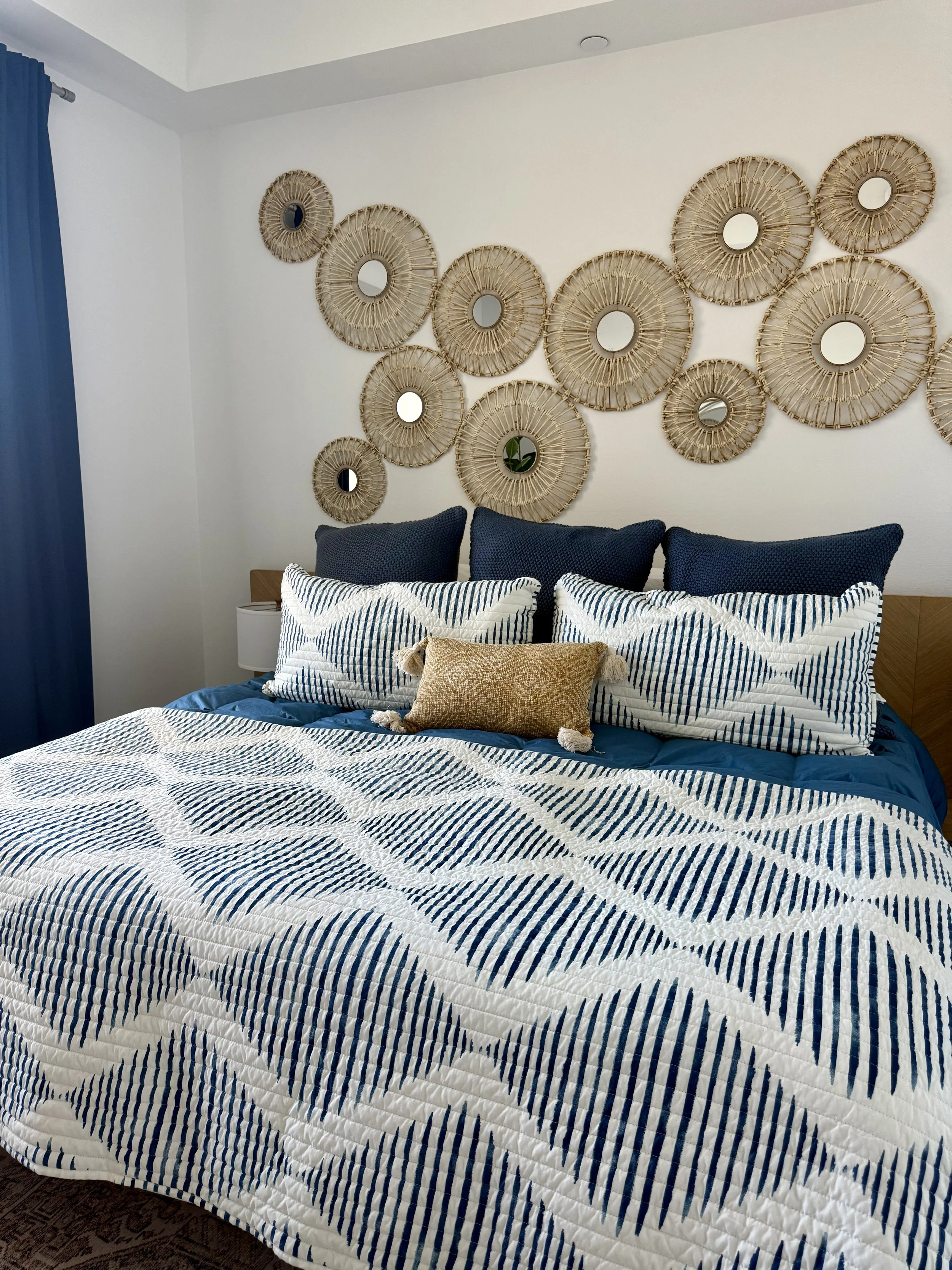 Coastal guest bedroom with blue and white bedding, woven wall art, layered textiles, and relaxed beach-inspired styling.