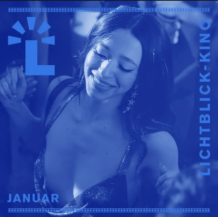A woman with long dark hair smiling and looking down, wearing a sleeveless top with metallic straps at a lively event or party.