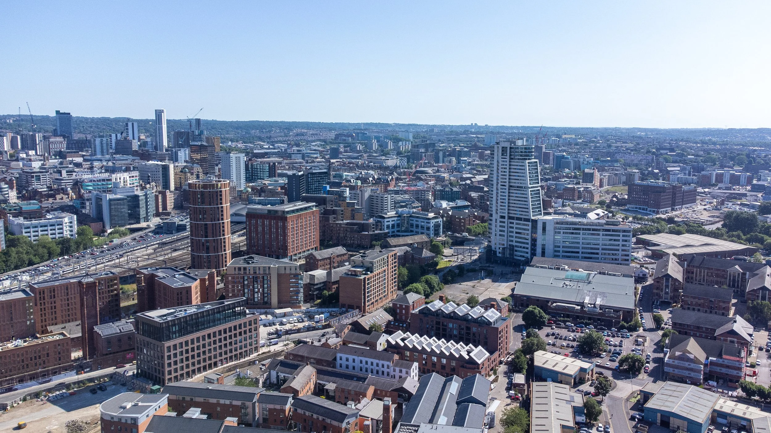 A panoramic aerial view of a city skyline with various modern high-rise buildings, office complexes, and streets on a clear, sunny day.