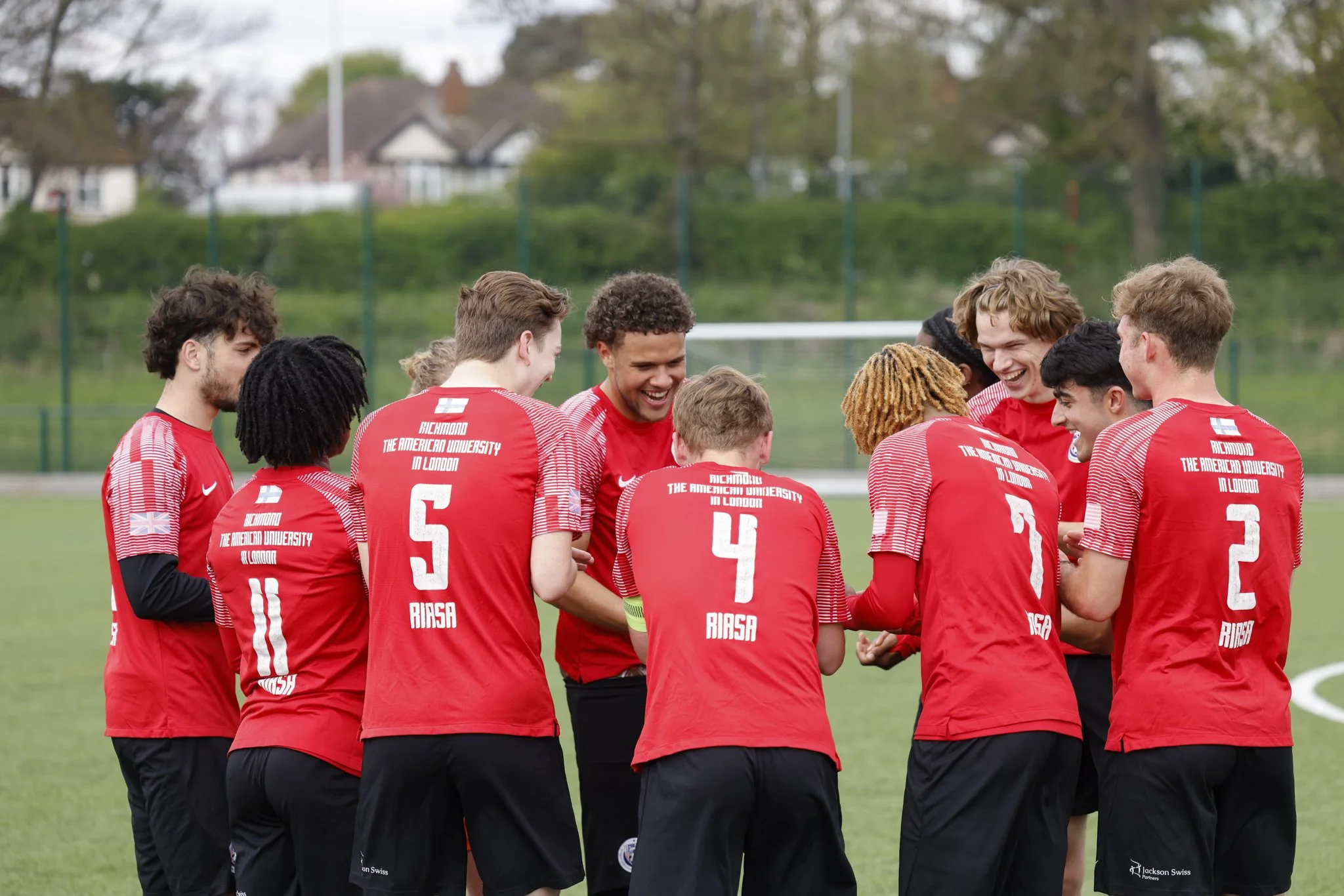 A group of soccer players wearing red jerseys huddling together on a field, smiling and engaging in team celebration or cheer.