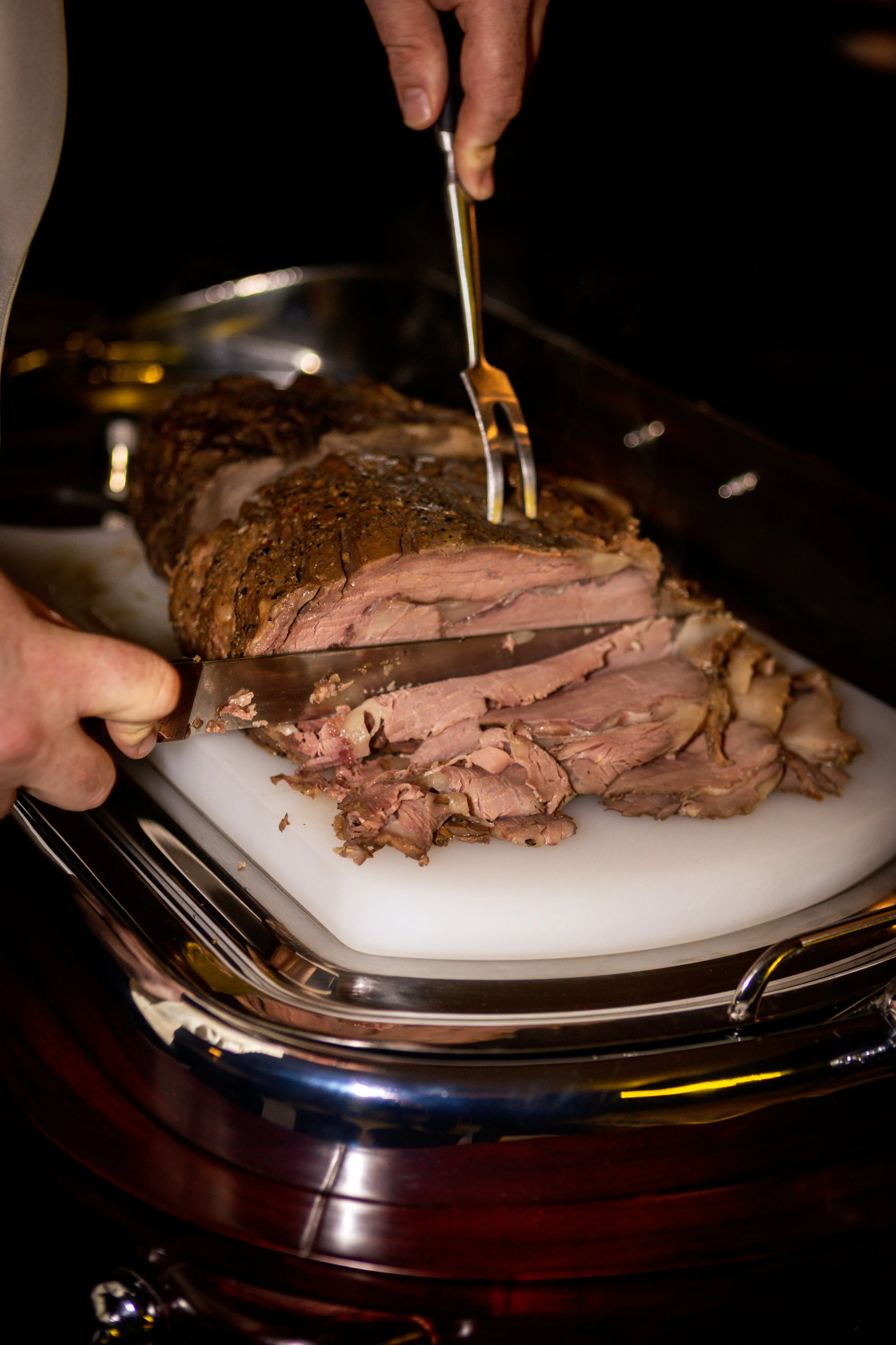 Person slicing a large cooked beef roast on a white cutting board.