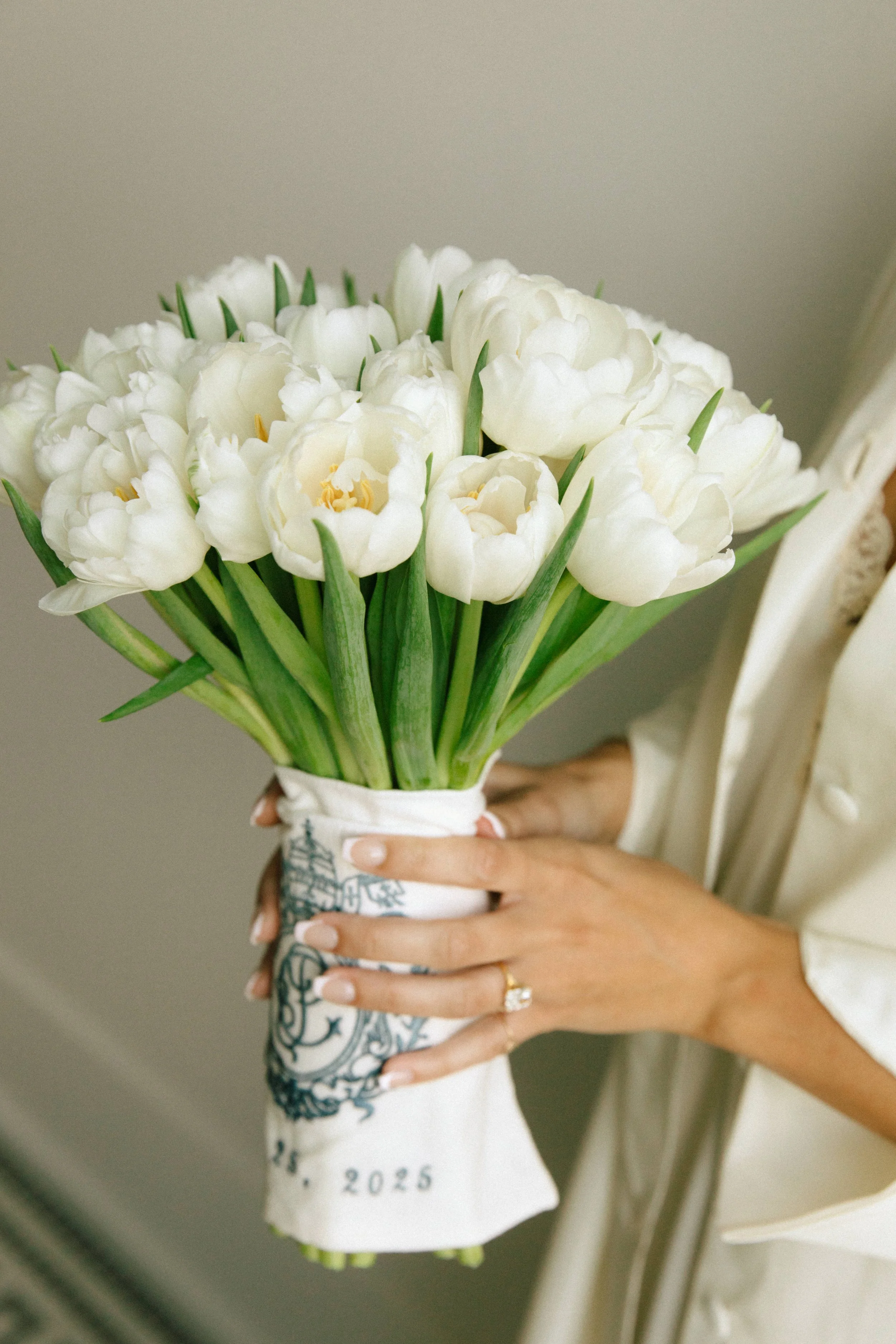 Person holding a bouquet of white tulips wrapped in a white cloth.