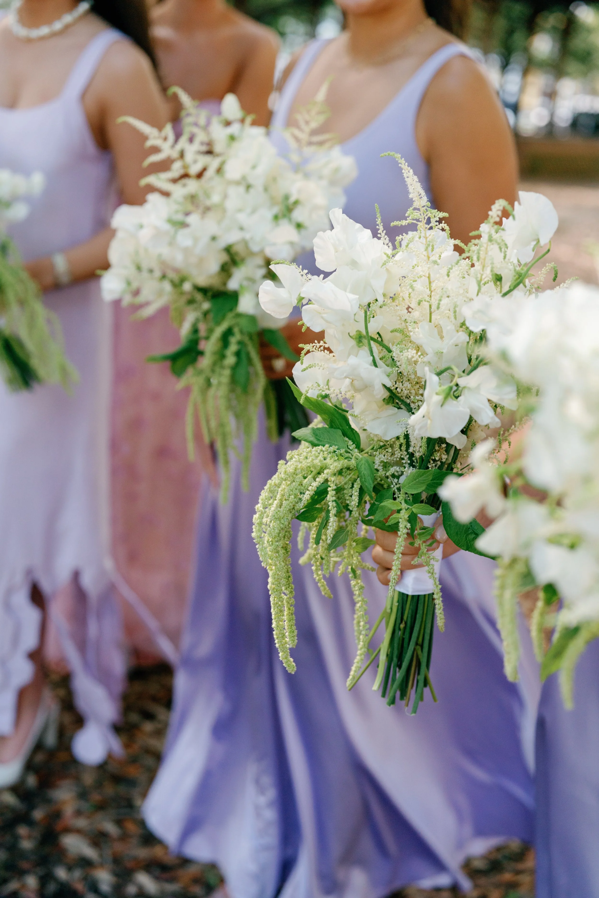 Bridesmaids holding bouquets of white flowers in pastel-colored dresses at a wedding.