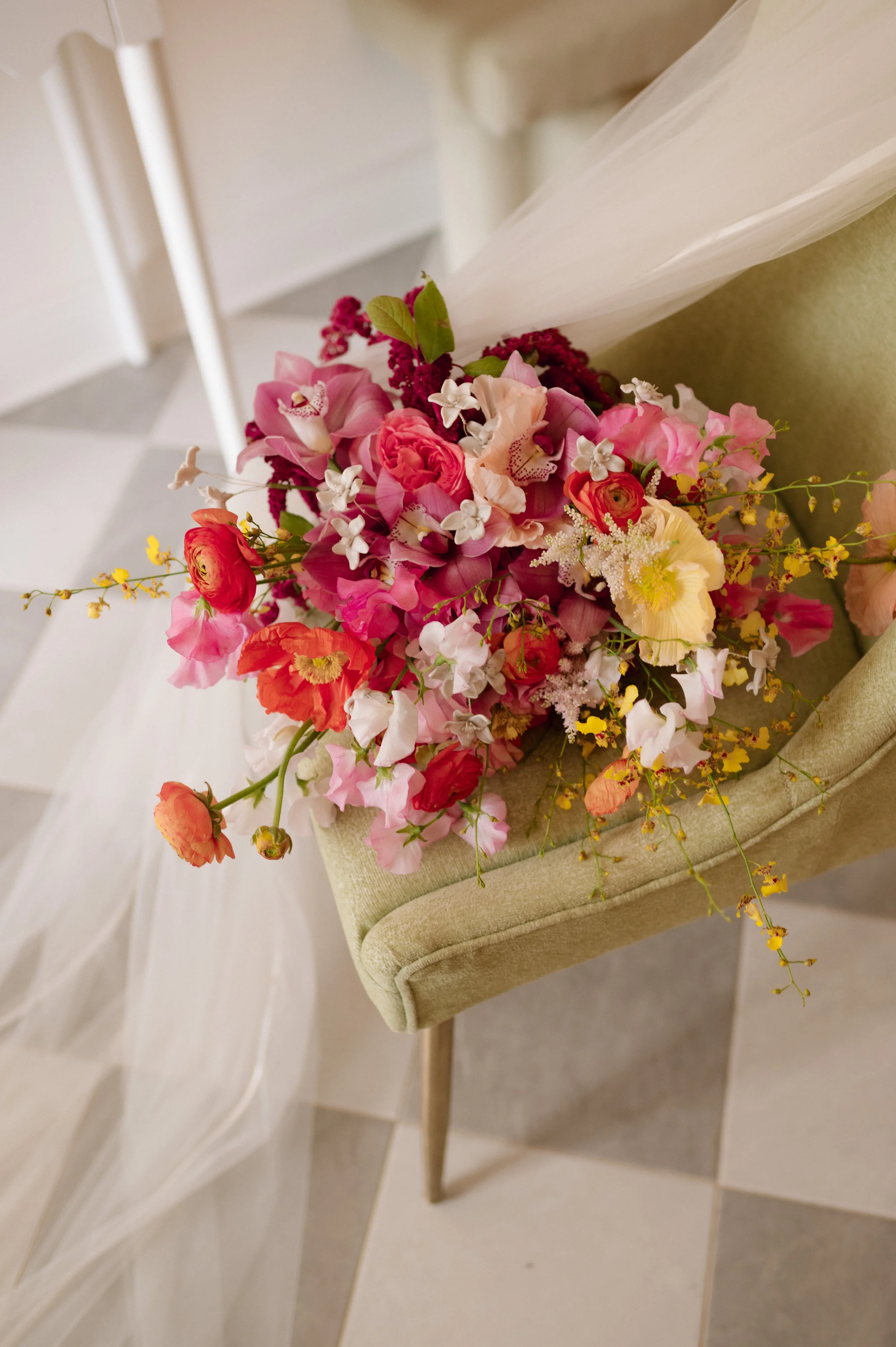 A colorful bouquet of pink, red, and yellow flowers resting on a green upholstered chair with wooden legs.