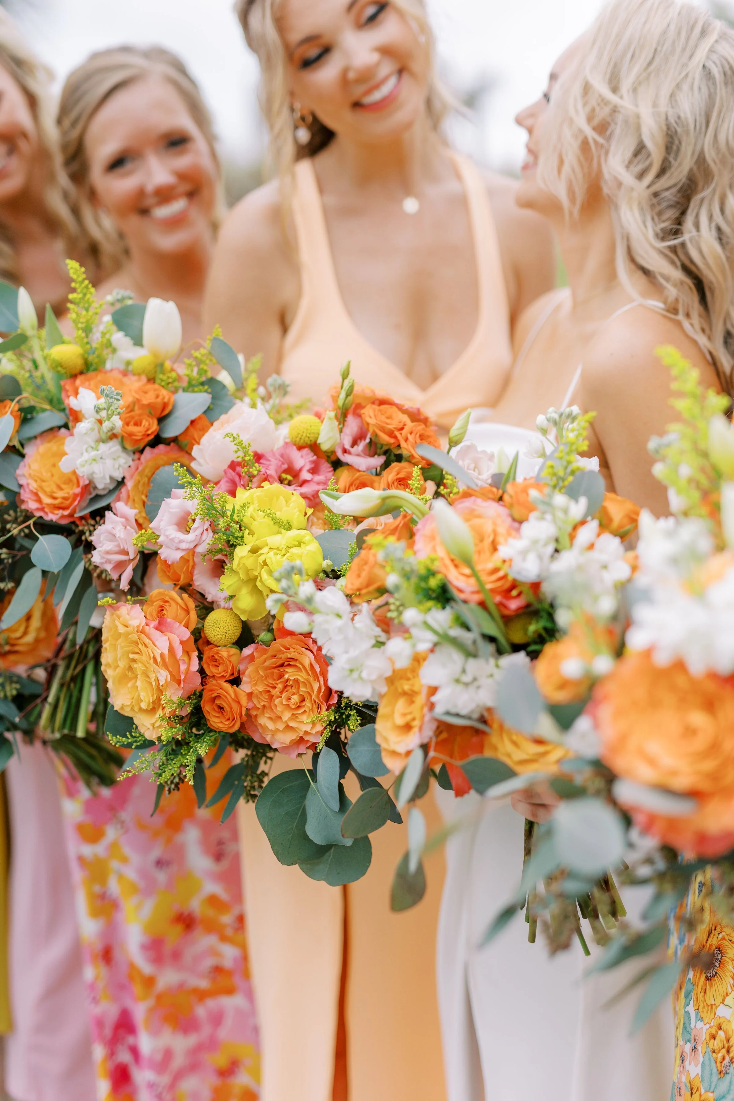 A group of women holding large, colorful floral bouquets at a wedding or celebration.