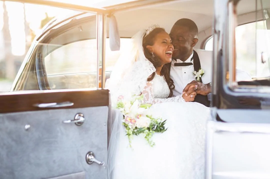 Happy bride and groom sitting in a vintage car, embracing and smiling after their wedding ceremony.