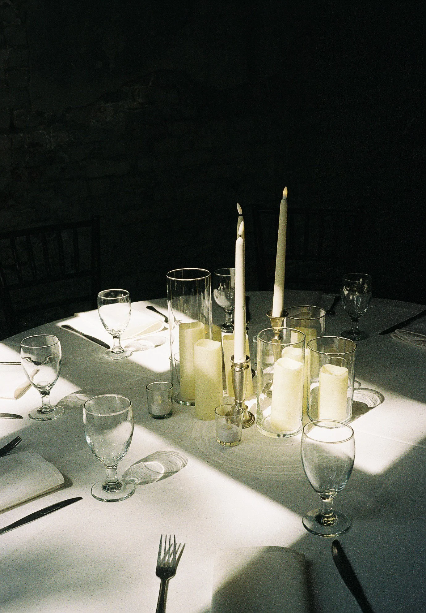 Elegant dining table with lit candles, glassware, and silverware, set for a formal meal in a dimly lit room.